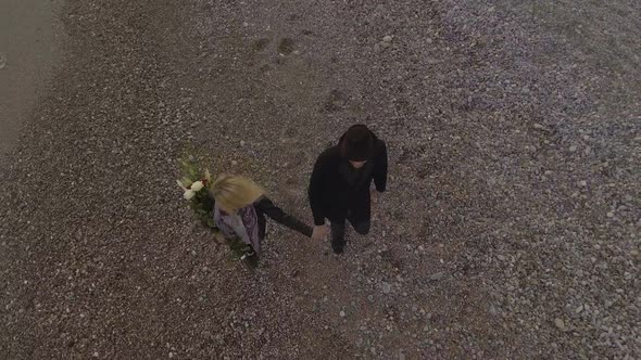 Young couple holding hands while walking by seashore, woman with flowers, love