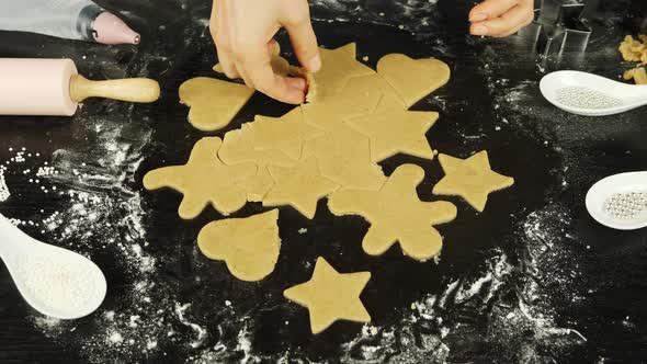 Female hands make gingerbread cookies in different shapes from rolled dough 