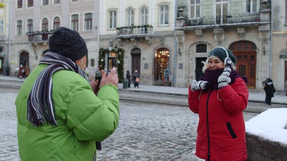 Senior Couple Man Woman Tourists Grandfather Taking Photo Pictures of Grandmother on Retro Camera