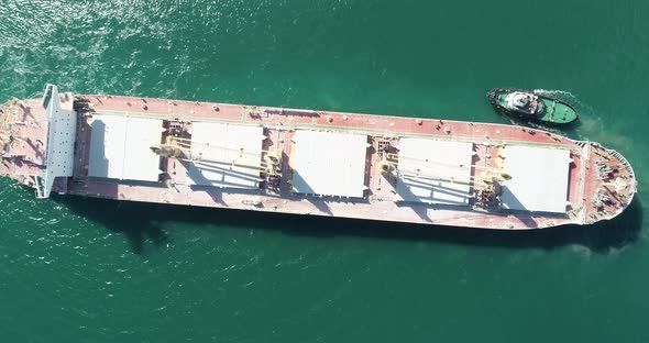 Large cargo ship enters the port escorted by tugboats.