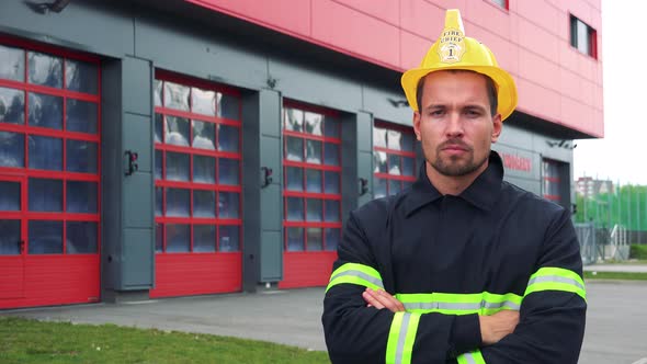 A Young Firefighter Looks at the Camera with Arms Folded Across His Chest, a Fire Station