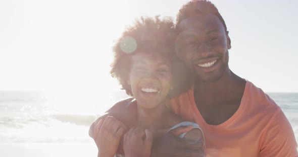 Portrait of smiling african american couple embracing on sunny beach