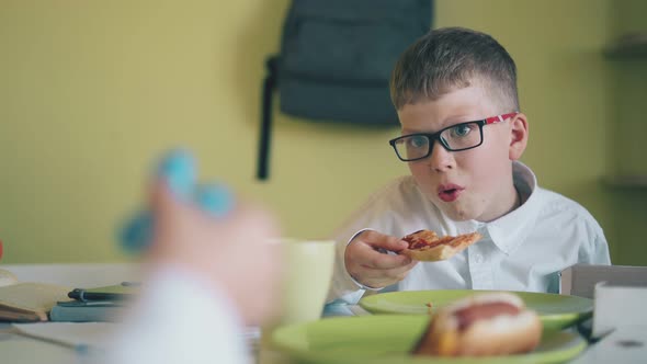 Boy Eats Pizza Looking at Classmate with Spinner at Table