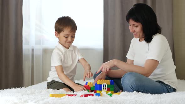 Happy Family: Mother and Son Play Building a House of Colored Blocks. The Child and Mother Play