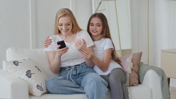 Mother with Teenage Daughter Child Girl Sitting Cuddling Looking at Screen of Mobile Phone Laughing
