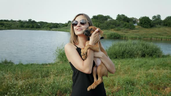 Woman Holds and Hugs a Small German Boxer Puppy in Nature