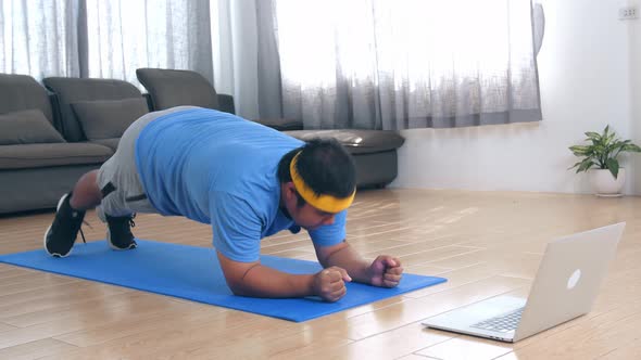 Overweight Man Struggling To Do Plank While Watching Online Tutorial On Laptop