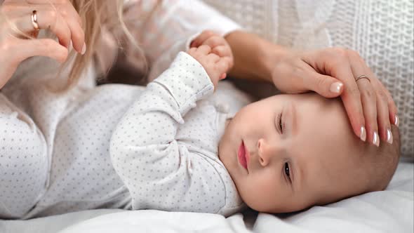 Closeup Caring Mother Hand Stroking Head of Cute Baby Lying on Bed