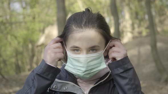 Serious Young Woman Putting on Face Mask and Looking at Camera. Close-up Portrait of Brunette Grey