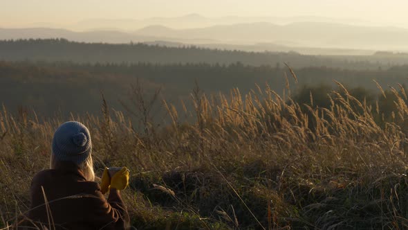 Beautiful girl with mug of tea in mountains Sudetes in November in sunset