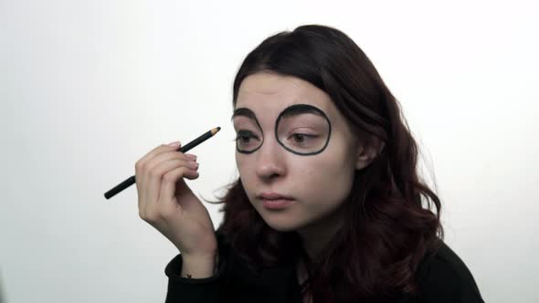 Woman Using Pencil to Draw Black Circles to Make Santa Muerte Makeup