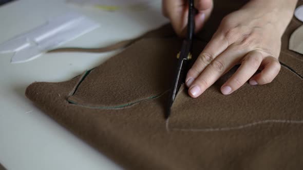 Close View of Female Hands Cutting a Brown Fabric with Scissors on Table in Atelier