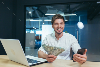  office looking at camera and smiling rejoices, holding phone and cash dollars income