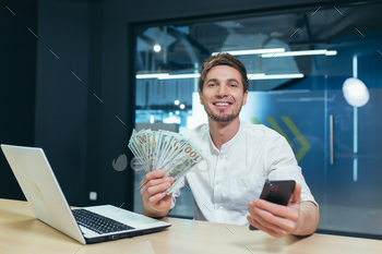  office looking at camera and smiling rejoices, holding phone and cash dollars income