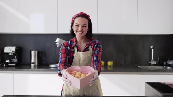 Smiling Woman in Apron Presents Box with Macaroons Cookies at the Kitchen