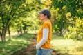 Portrait of female farm worker wearing orange t-shirt and trucker's hat in walnut tree orchard - PhotoDune Item for Sale