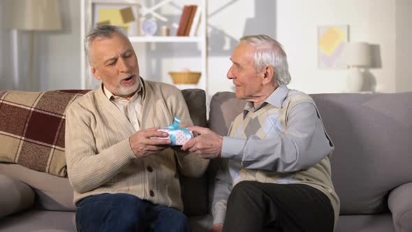 Aged Man Presenting Birthday Gift Box to Smiling Friend, Celebration at Home