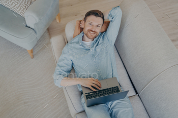 mmission early, lying  on comfortable couch in living room, resting head on hand, looking up while smiling and being satisfied