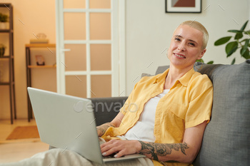 miling at camera while buying purchase online on laptop sitting on sofa