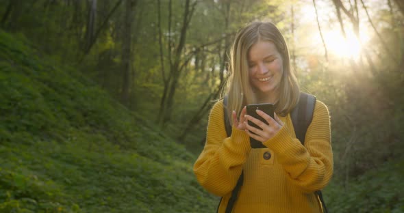 The Girl Is Looking at the Maps on the Smartphone and Goes Through the Forest