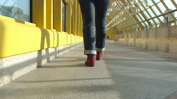 Women's Legs in Burgundy Boots and Blue Jeans Walk on a Closed Pedestrian Bridge