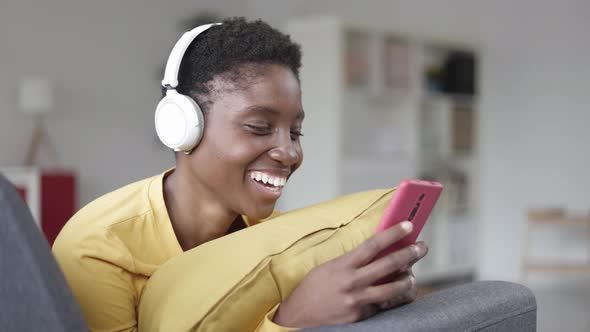 Happy Black Young Woman Using Smart Phone While Lying on Sofa at Home