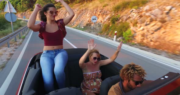 Attractive brunette dancing while sitting on hood of convertible