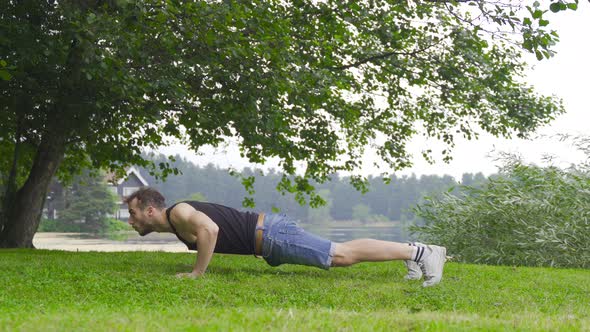 Athlete man doing push-ups by lake in nature.