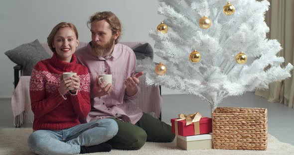 Young Couple Drinking Cocoa Cappuccino Tea While Sitting at Cozy Home on Floor Near Christmas Tree