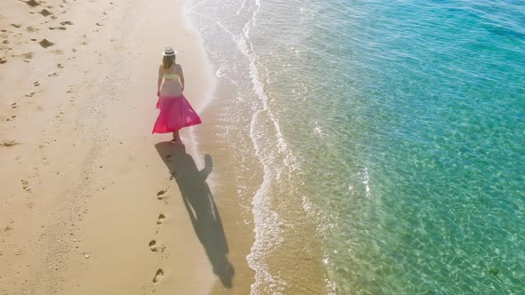 Happy Woman in Pink Beach Dress Walking By Scenic Tropical Ocean Beach at Sunset
