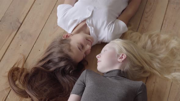 Two Girlfriends Lying on the Wooden Floor Looking at Each Other