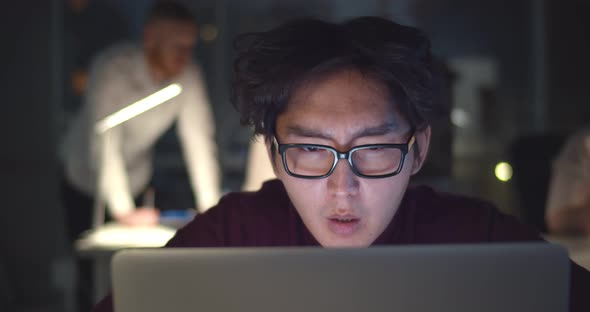 Focused Asian Office Employee Looking at Laptop Working in Office at Night