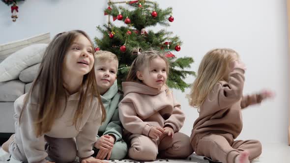 Playful Children Sit Near the Christmas Tree