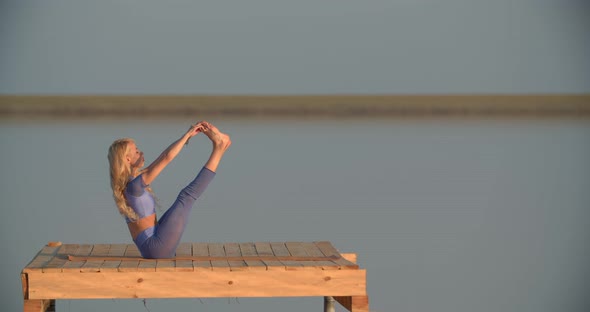 Woman is Sitting on a Wooden Platform in the Lake and Stretching Her Legs