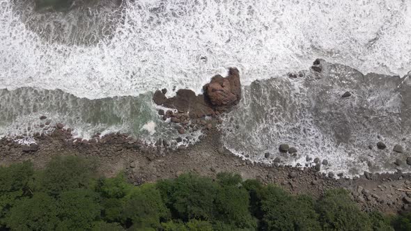 Birds eye view aerial shot of ocean waves crashing into rocks on the shore