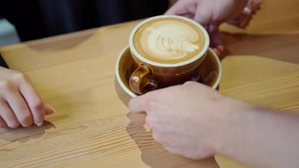 Barista's Hands Bring a Brown Mug of Cappuccino Coffee with Beautiful Latte Art to the Client's