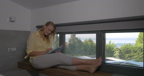 Smiling Woman with Tablet on Window Sill