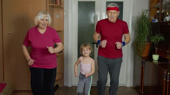 Granddaughter and Mature Grandparents in Sportswear Making Sports Jogging Workout Exercises at Home