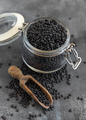 Glass jar of dry black lentils beans with a scoop on grey table close up,  healthy protein diet - PhotoDune Item for Sale