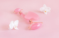 Facial roller and gua sha massager near white orchid flowers on light pink, close up - PhotoDune Item for Sale