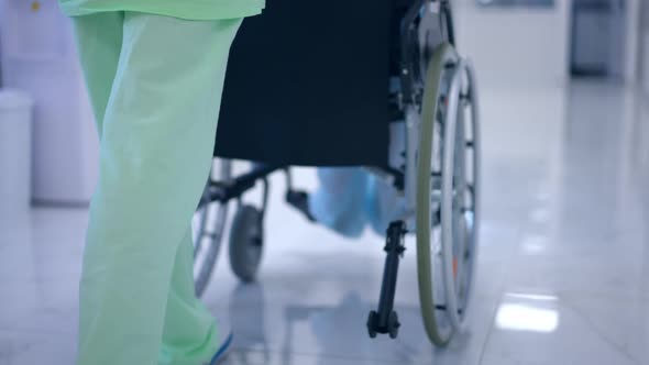 Tracking Shot of Unrecognizable Woman in Medical Uniform Pushing Wheelchair with Patient in Hospital