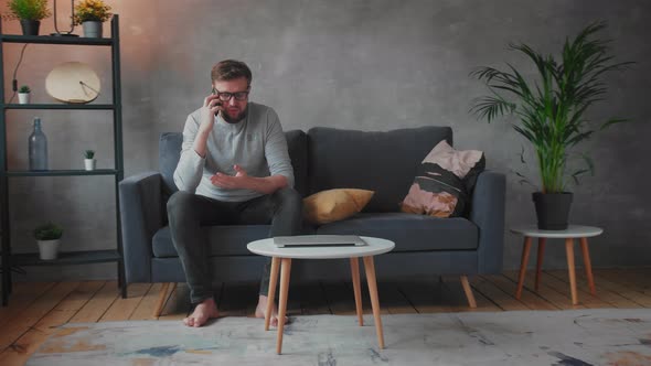 Young Man in Glasses Angry Talking on the Phone Sitting on the Couch