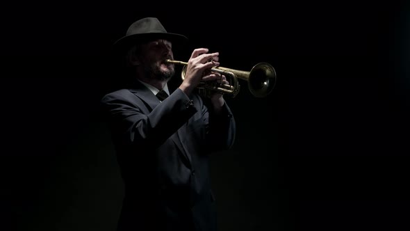 Man Musician in Hat and Formal Suit Plays Trumpet on Black Background Front View