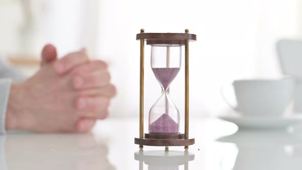 Hourglass on a Table Near Hands of a Man Waiting Impatiently 