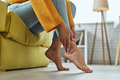 Close-up of woman massaging her tired feet while sitting on the couch at home - PhotoDune Item for Sale
