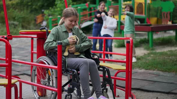 Crying Desperate Caucasian Girl in Wheelchair Hugging Toy As Blurred Children Pointing Laughing at