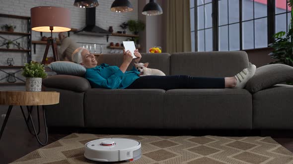 Cheerful Elderly Woman Lying on Sofa with Tablet