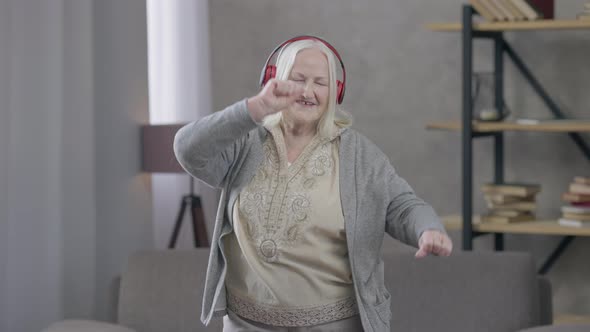 Relaxed Positive Retiree in Headphones Dancing to Music in Headphones Smiling