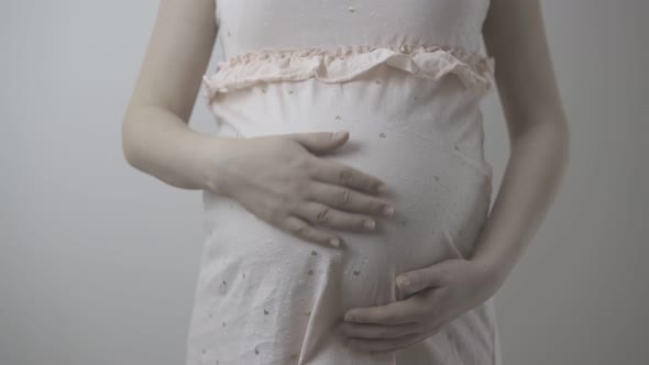 Future Mother in Pink Dress Strokes Tummy at Wall Closeup