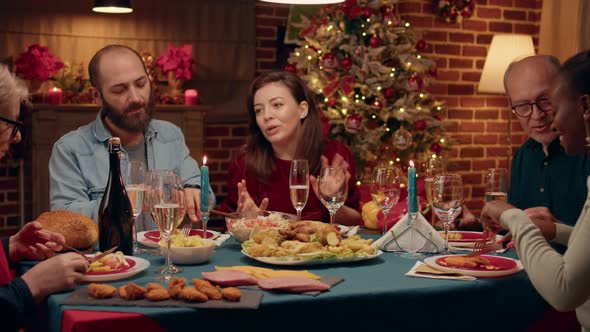 Happy Wife Talking to Guests About Food While Sitting Together at Christmas Dinner Table